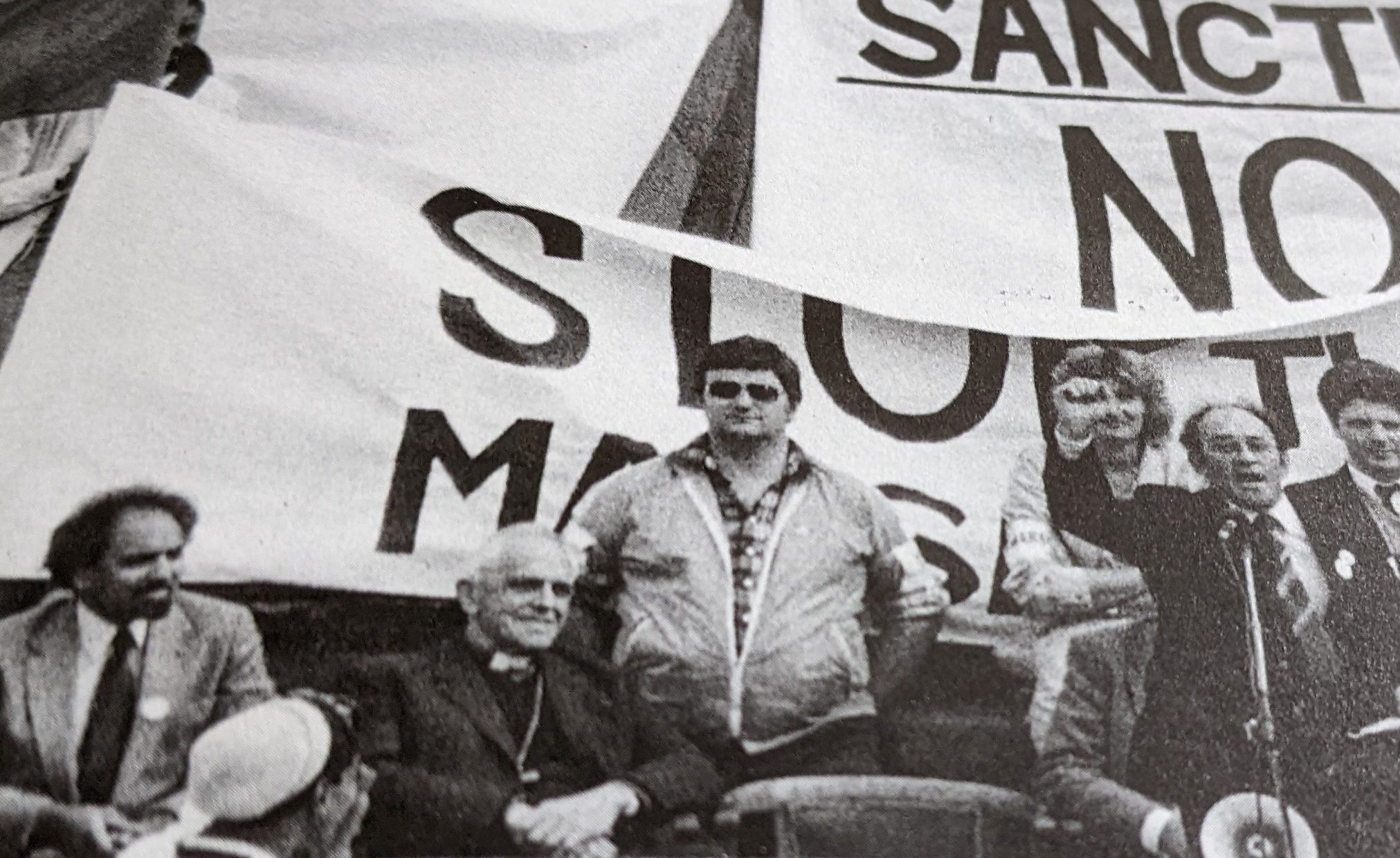 Dennis Goldberg speaking, Jerry Herman and Bishop Huddleston left facing picture